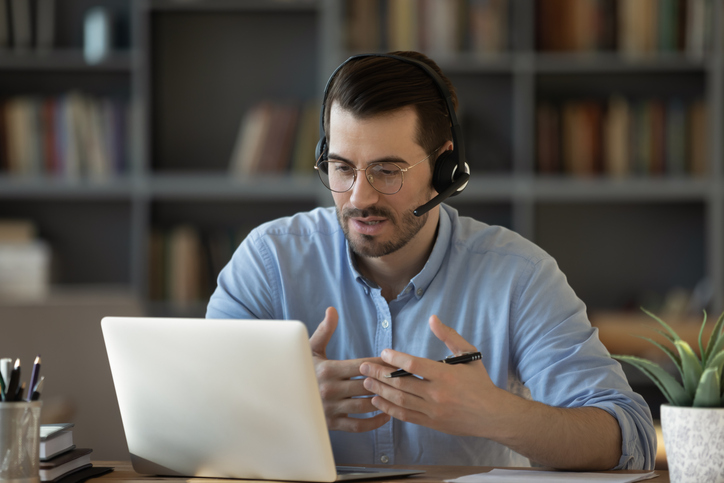 Confident man teacher wearing headset speaking, holding online lesson